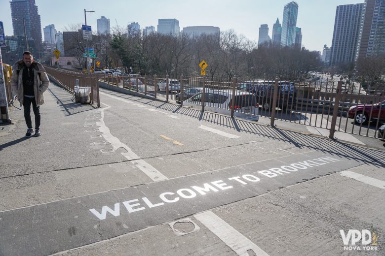 Fora de Manhattan, Brooklyn é a região que mais faz sentido e com mais coisas legais para curtir. Foto de um escrito que diz "Welcome to Brooklyn" no chão da rua, com os prédios e o céu de Nova York ao fundo 