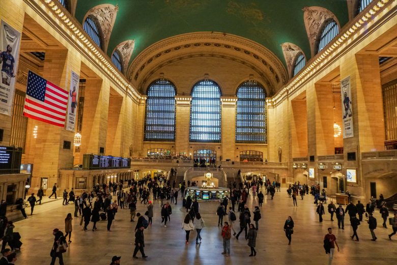 Foto do interior da estação Grand Central, em Nova York, com a cúpula alta pintada de verde e visitantes circulando