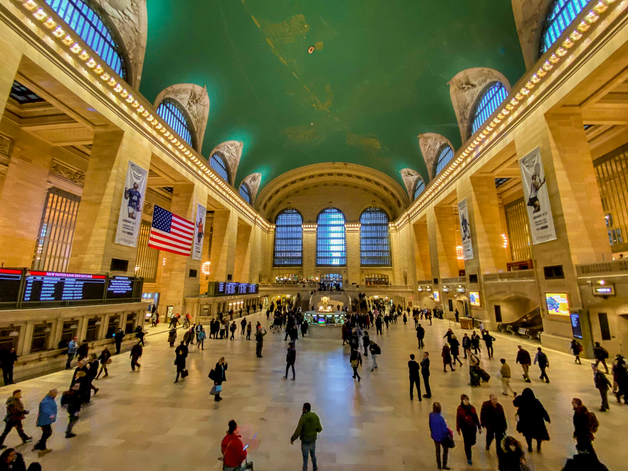 Foto do interior da estação Grand Central, em Nova York, com a cúpula alta pintada de verde e visitantes circulando