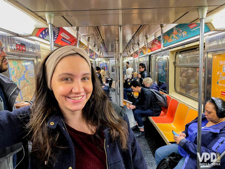 Foto da Rê sorrindo, em pé dentro do trem do metrô de NY