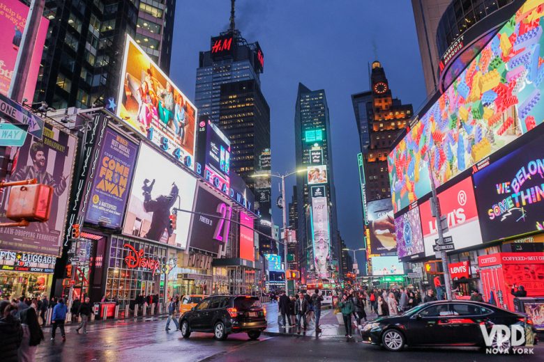 Foto da Times Square iluminada e cheia ao entardecer, com os prédios de Nova York ao fundo 