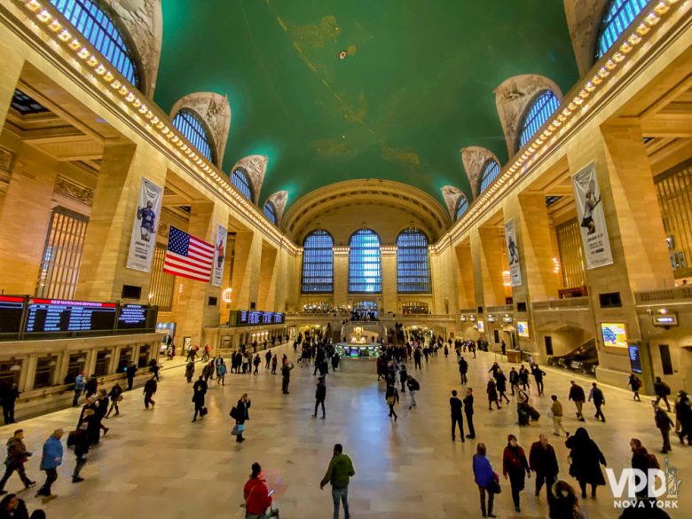 Foto do interior da estação Grand Central, em Nova York, com a cúpula alta pintada de verde e visitantes circulando