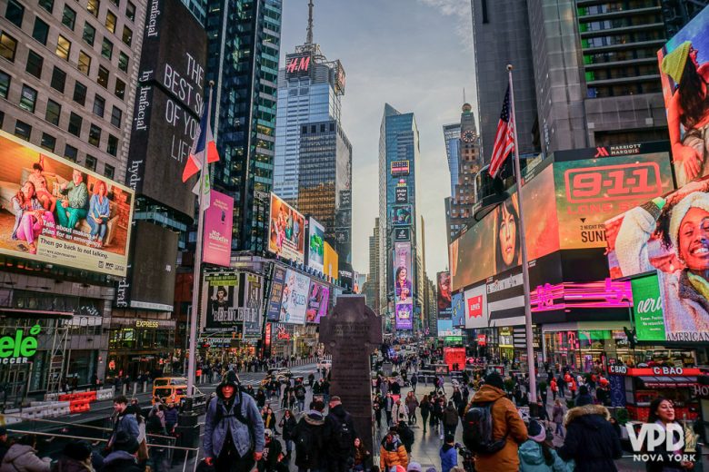 Foto da Times Square iluminada e cheia ao entardecer, com os prédios de Nova York ao fundo 