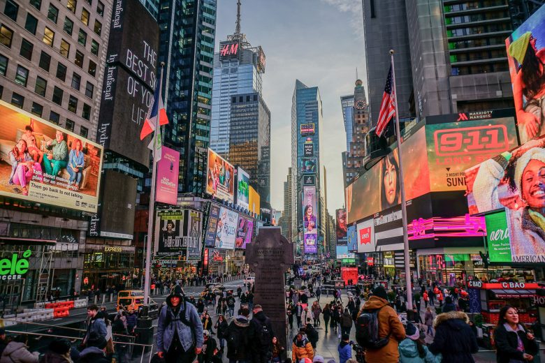 Foto da Times Square iluminada e cheia ao entardecer, com os prédios de Nova York ao fundo