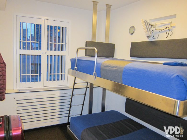 Foto do quarto e da beliche do The Pod 51, com roupa de cama azul e cinza listrada 