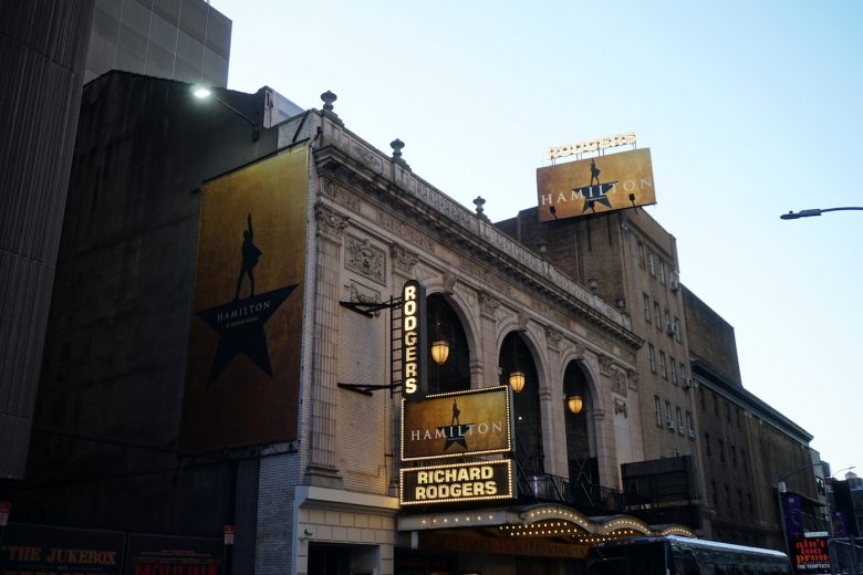 Foto da fachada da Broadway em Nova York, com cartazes do musical Hamilton em três pontos diferentes 