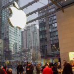 Foto de uma loja da Apple em Nova York, cheia de pessoas e com a maçã que é o logo em tamanho gigante sobre o vidro