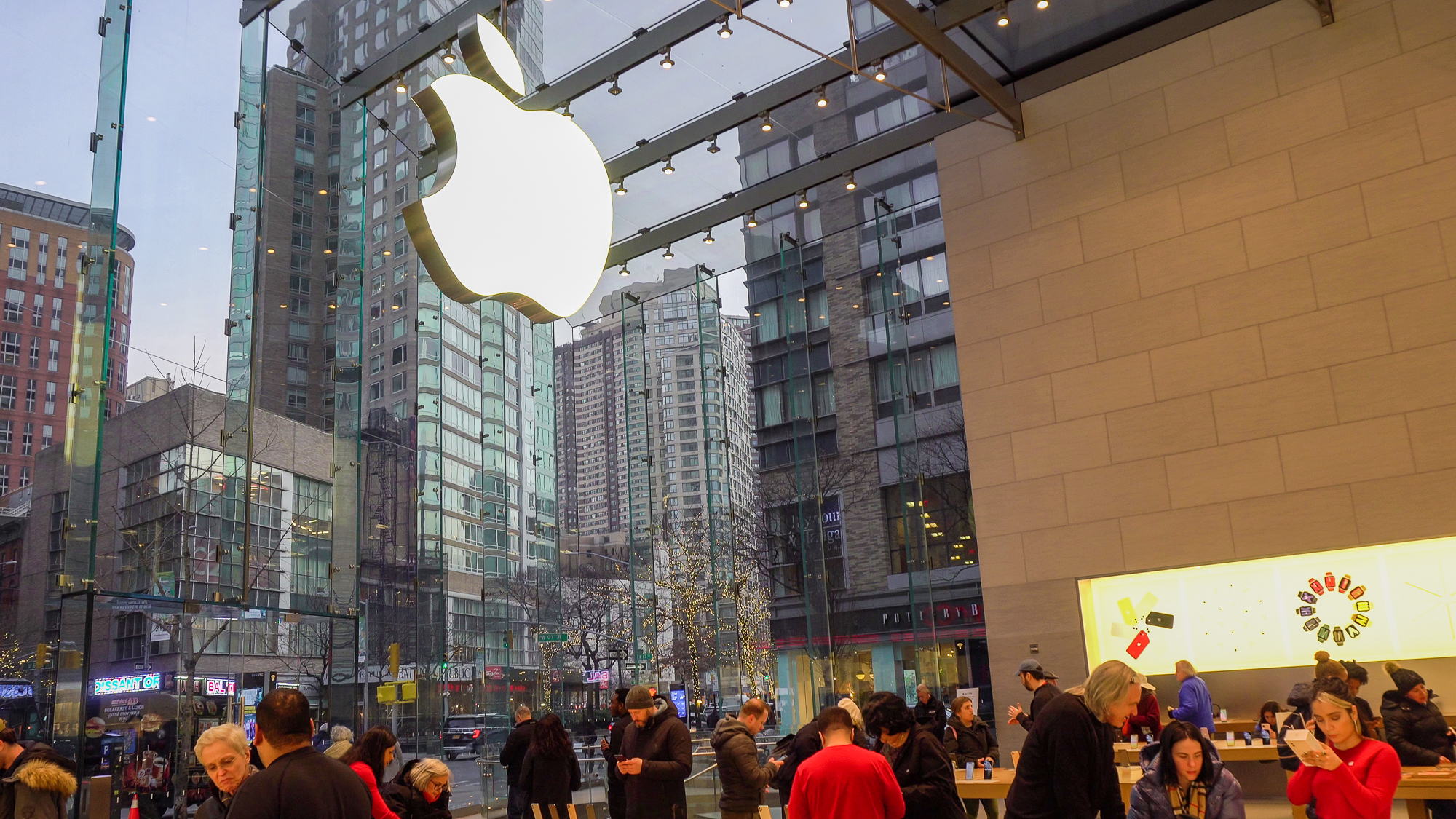 Foto de uma loja da Apple em Nova York, cheia de pessoas e com a maçã que é o logo em tamanho gigante sobre o vidro