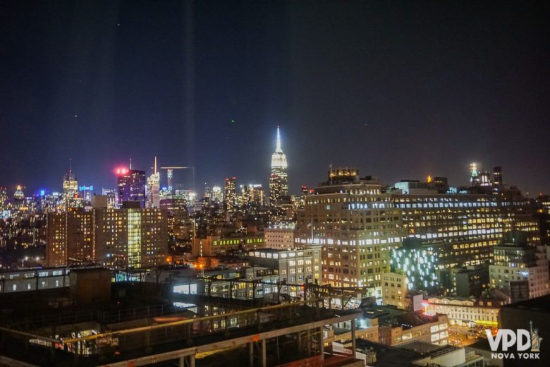 Foto da cidade de Nova York iluminada à noite, com o Empire State em destaque no fundo. 