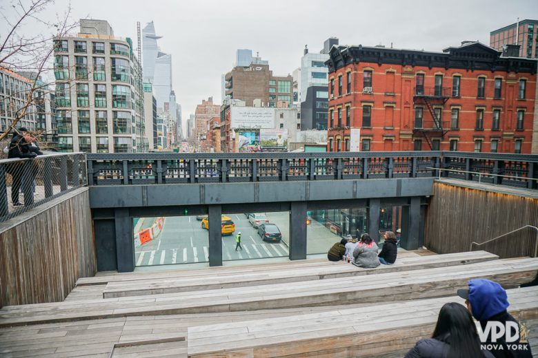 Foto de pessoas sentadas em uma plataforma de madeira no The High Line, com a cidade ao fundo 