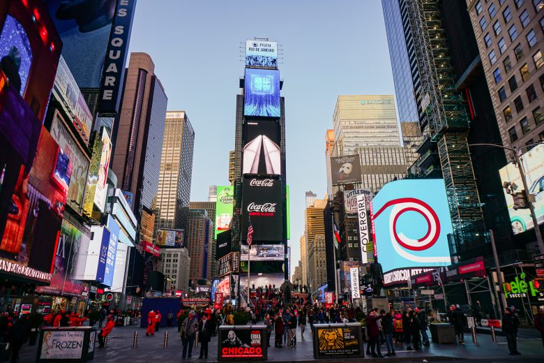 Foto da Times Square de Nova York durante o dia, com as lojas e os telões já começando a acender