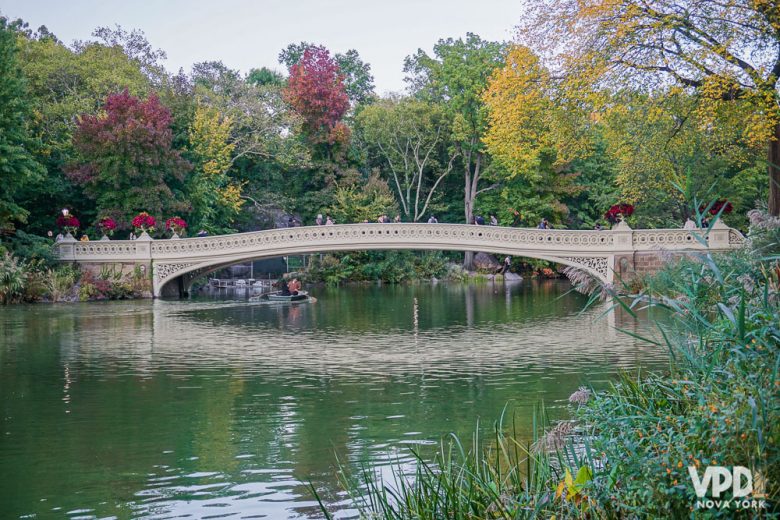 Foto da ponte do Central Park com árvores com folhas verdes, vermelhas e amarelas ao redor 