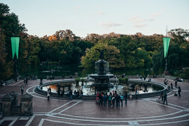 Foto de uma fonte no Central Park, com árvores ao redor e visitantes passeando pelo parque.