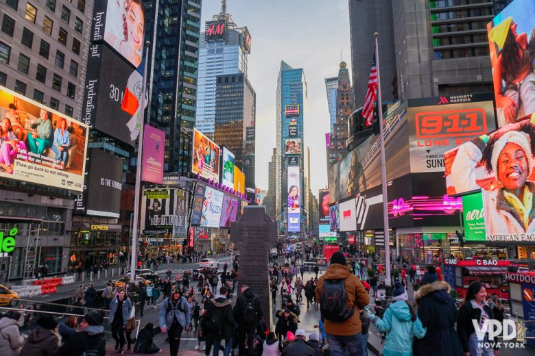 Foto da Times Square de Nova York durante o dia, com as lojas e os telões já começando a acender. Os personagens da Times Square são medonhos para adultos e mais ainda pra crianças