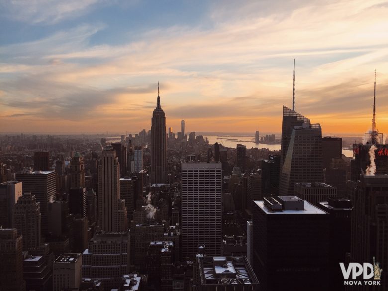 Entenda todas as condições do seguro viagem oferecido pelos cartões de crédito. Foto da cidade de Nova York no pôr do sol, com os prédios escuros e o céu azul, rosa e laranja