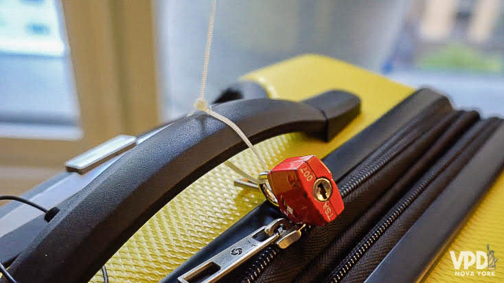 Foto de uma mala amarela, fechada com cadeado no zíper 