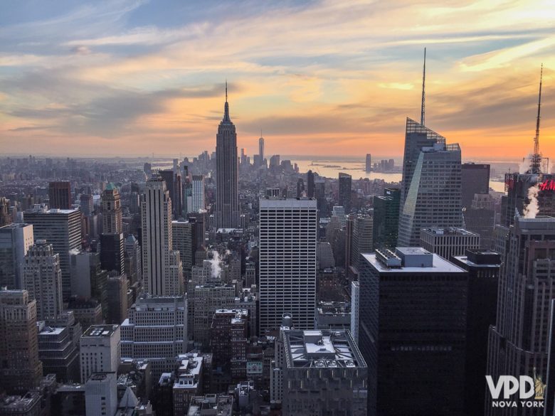 Dá pra ficar perdido com todas as opções de atrações em Nova York. Foto da cidade de Nova York no pôr do sol, com os prédios escuros e o céu azul, rosa e laranja