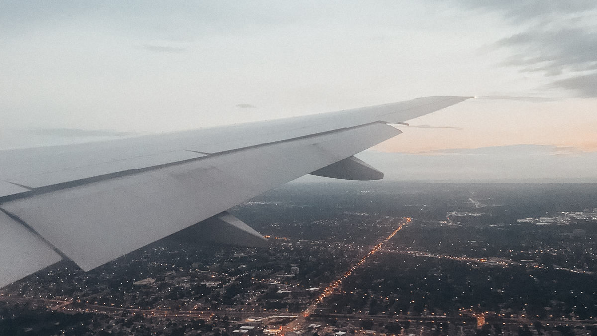 Foto da asa de um avião sobrevoando a cidade de Nova York, com um céu cinza-claro ao fundo