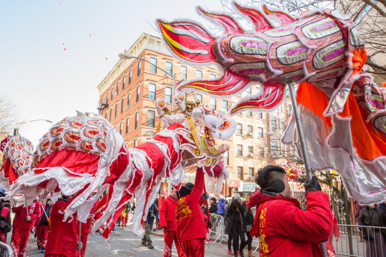 Imagem da parada do Ano Novo Lunar, que acontece em fevereiro. Várias pessoas vestidas de vermelha caminham segurando fantoches de dragões.