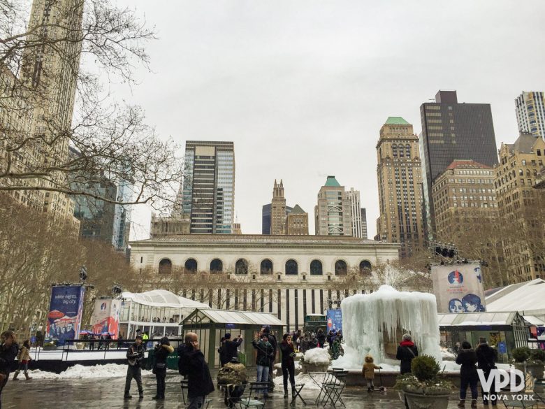 Imagem mostrando o Bryant Park em fevereiro. Ele está mais vazio, e algumas pessoas caminham no parque Há prédios ao fundo e uma fonte congelada.