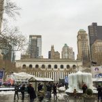 Imagem mostrando o Bryant Park em fevereiro. Ele está mais vazio, e algumas pessoas caminham no parque Há prédios ao fundo e uma fonte congelada.