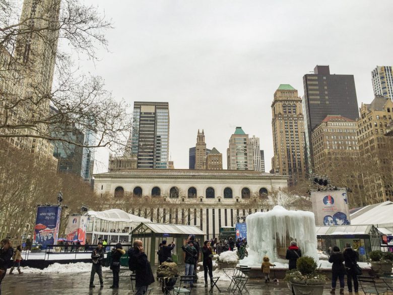 Imagem mostrando o Bryant Park em fevereiro. Ele está mais vazio, e algumas pessoas caminham no parque Há prédios ao fundo e uma fonte congelada.