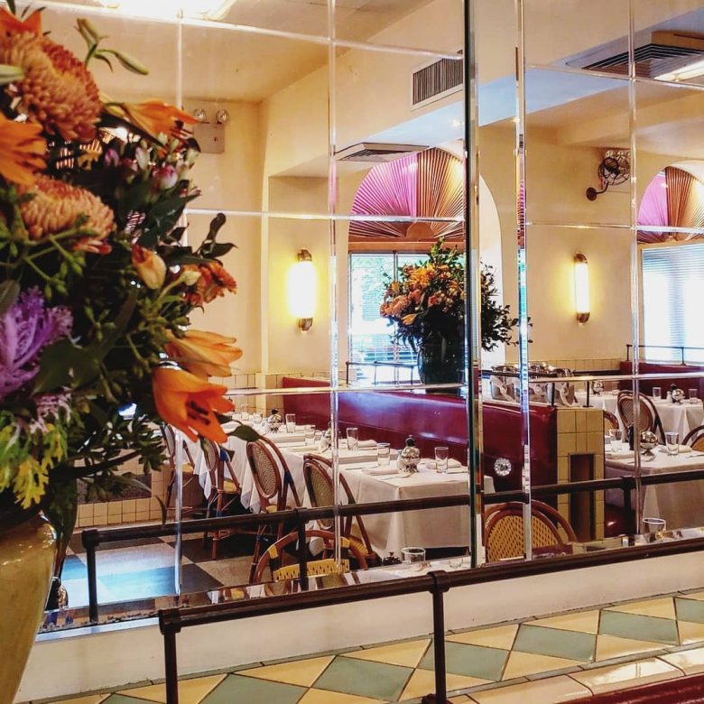 Foto de um espelho que mostra a configuração do restaurante. As mesas são bem juntas e há arranjos de flores espalhados.