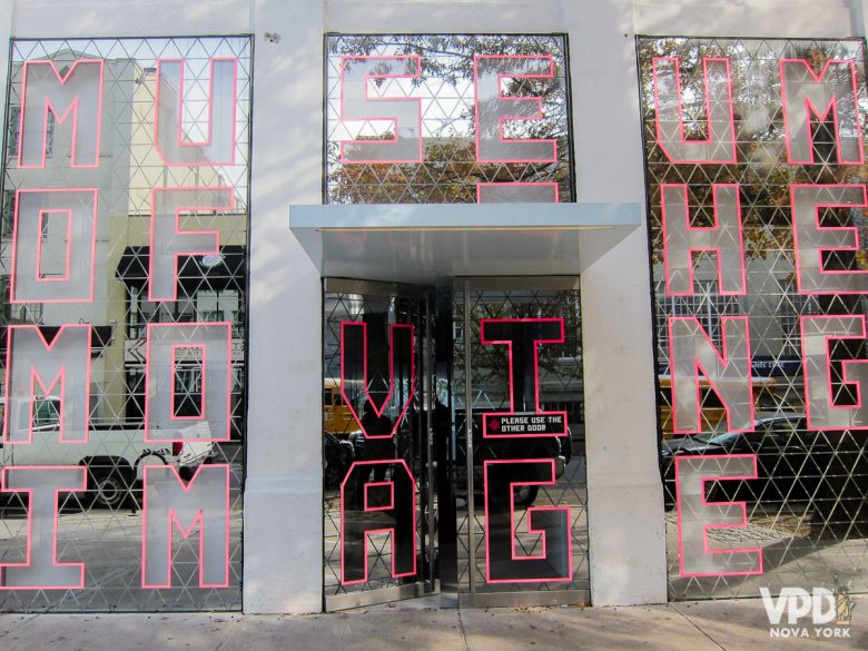 Foto da entrada do Museum of Moving Image, com letras em vermelho em uma estrutura espelhada.