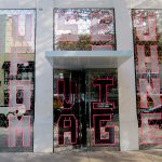 Foto da entrada do Museum of Moving Image, com letras em vermelho em uma estrutura espelhada.