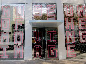Foto da entrada do Museum of Moving Image, com letras em vermelho em uma estrutura espelhada.