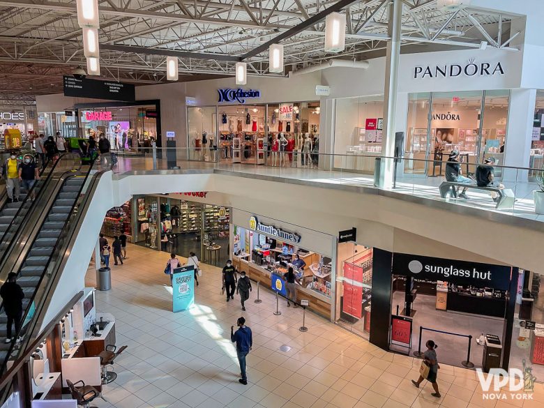 Foto tirada do segundo andar do Jersey Gardens. Há lojas da Pandora, sunglass hut, Auntie Anne's e pessoas andando, além de uma escada rolante do lado esquerdo.