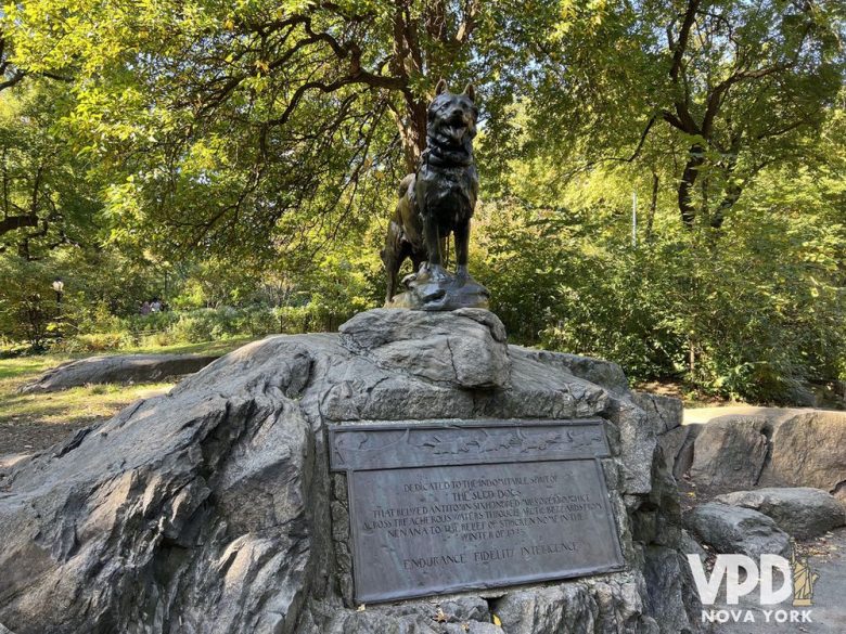 Foto da escultura do cachorro Balto, em meio há várias árvores.