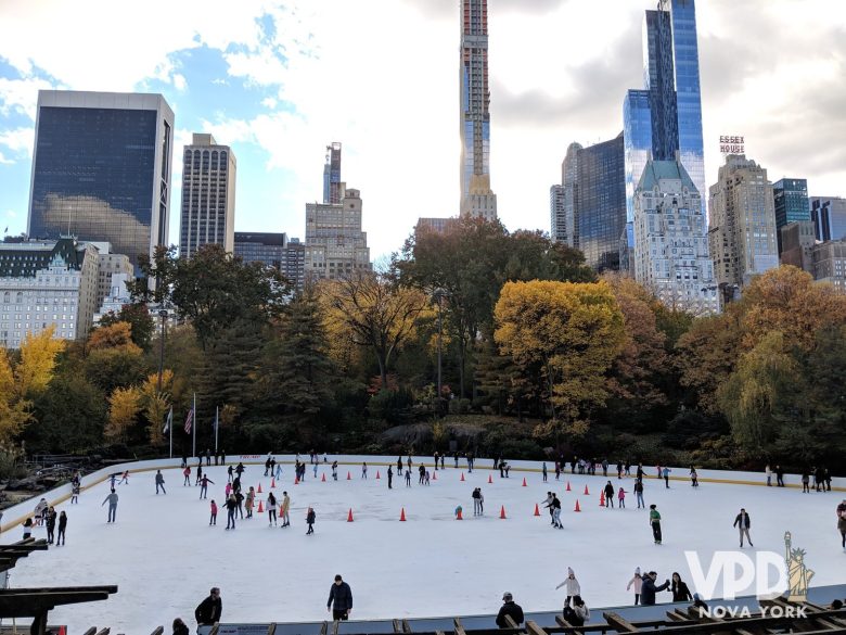 Foto da pista de patinação do Central Park. Há várias pessoas patinando, cones laranjas no centro e vários prédios e árvores ao redor.